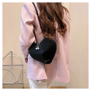 Détail du sac à bandoulière noir en forme de cœur avec pendentif papillon sur modèle