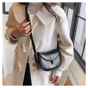 Dettaglio borsa a sella nera con fibbia argentata indossata su un lungo cappotto beige