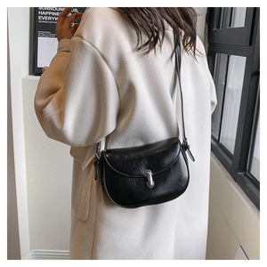 Dettaglio di borsa a sella nera in pelle con fibbia argento indossata su cappotto tweed