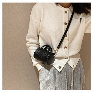 Detail of black pebbled leather cylinder bag with gold hardware and side logo embossing