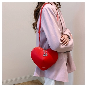 Détail du sac à bandoulière en cuir rouge en forme de cœur avec breloques trèfle