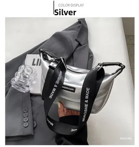 Close-up of silver crescent bag with metallic finish and wide branded webbed strap
