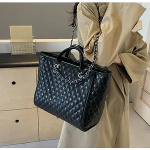 Detail of black quilted tote bag with chain strap and leather handle in a lifestyle setting
