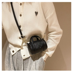 Detail of black lychee grain leather mini cylindrical bag with gold metal hardware