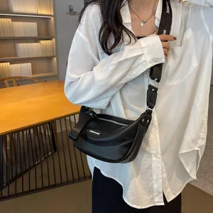 Detail of a black crescent crossbody bag featuring a wide logo strap on a casual model