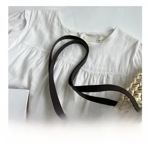 Detail of soft pleated cotton fabric with smooth dark brown leather shoulder strap