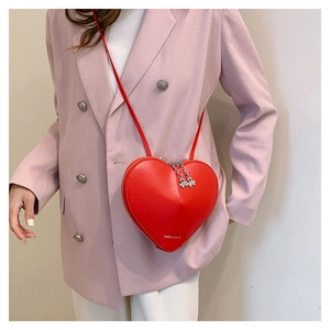 Détail d'un sac bandoulière rouge en forme de cœur avec fermetures éclair et cuir mat