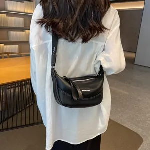 Close-up of black PU leather dumpling bag with wide logo strap in a modern room