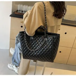 Close-up of quilted black tote bag with silver chain strap worn by a model