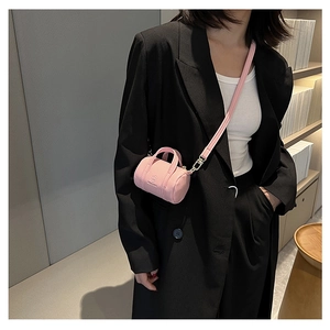 Detail of pink cylindrical mini bag in pebbled leather worn by model on shoulder