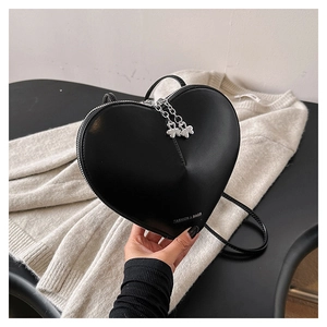 Détail d'un sac en forme de cœur noir avec fermeture trèfle argentée sur un tricot blanc