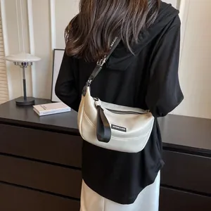 Detail of cream crescent crossbody bag with woven strap shown on a model's shoulder