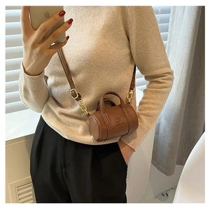 Close-up of a mini cylindrical crossbody bag in dark brown leather with gold metal hardware