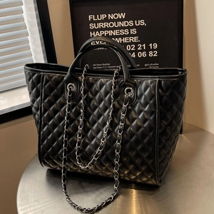 Black quilted tote bag with diamond pattern and metal chain strap on industrial table