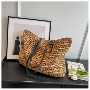 Detail of woven straw tote bag with brown leather handles on a minimalist art desk