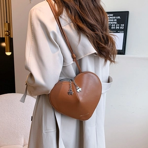 Sac bandoulière marron en forme de cœur avec pendentif trèfle porté par un mannequin
