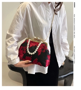 Détail d'un sac à main en satin noir avec broderie florale rouge et anse en perles