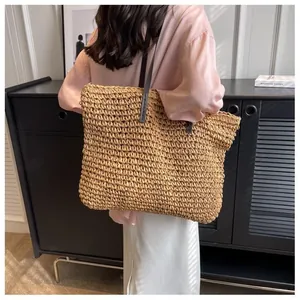 Detail of a large woven straw tote bag with brown straps styled on a model for beach fashion