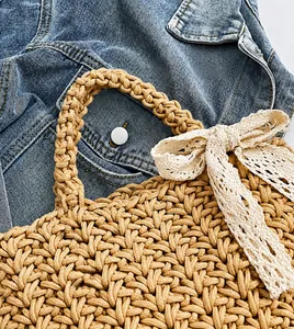 Close-up of handmade straw woven handbag featuring cream lace bow and thick rope texture