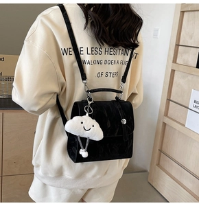 Detail of a shiny black square backpack with a cute white plush cloud charm for women