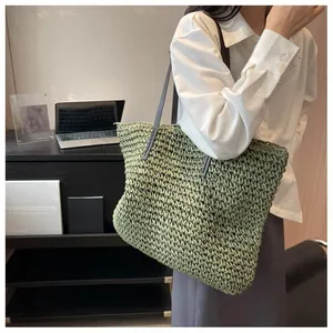 Detail of green woven straw tote bag with long grey shoulder strap on a female model