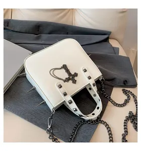Close-up of white gothic handbag with silver spikes, pyramid studs and cross pendant