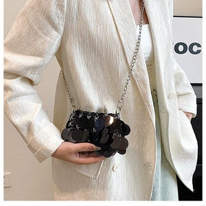Close-up of mini black sequined shoulder bag with silver metal chain on a white blazer