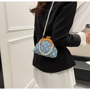 Detail of blue denim mini bag with butterfly embroidery and pearl chain strap on model