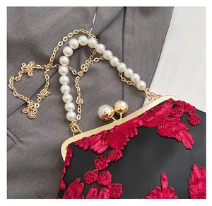 Détail du sac en satin noir avec broderie florale rouge et poignée en perles chic