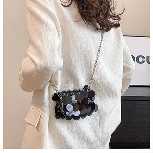 Detail of a mini black sequin bag with silver chain strap worn on white blazer