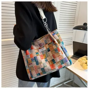 Model wearing a large colorful plaid tote bag with chain strap in a cozy interior