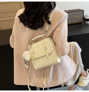 Detail of cream white faux leather backpack with plush puppy charm and metal buckles