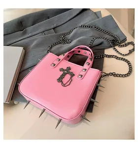 Detail of pink punk handbag featuring metal spikes, cross pendant, and silver chain strap