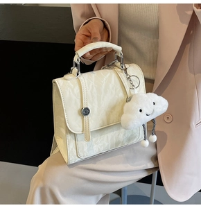 Detail of cream-white pleated handbag featuring a plush cloud charm and silver magnetic buckle