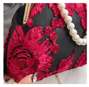 Détail de broderie florale 3D rouge sur tissu de soie noir avec poignée en perles