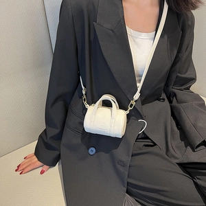 Minimalist off-white cylinder crossbody bag with litchi texture on a model in black