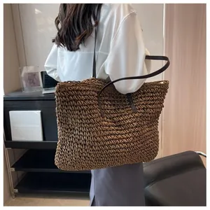 Detail of a large brown straw tote bag shown on a shoulder with textured woven finish