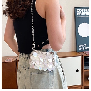 Detail of white iridescent sequin crossbody bag with silver chain strap on a model