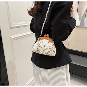 Detail of white fabric crossbody bag with floral embroidery and elegant pearl chain strap