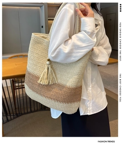Detail of a large woven tote bag featuring a two-tone design with a tassel and wood beads