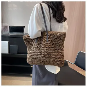 Detail of hand-woven straw tote bag with black faux leather straps on shoulder