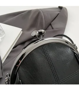 Macro shot of silver kiss lock clasp on black faux leather shell bag with cross stitching
