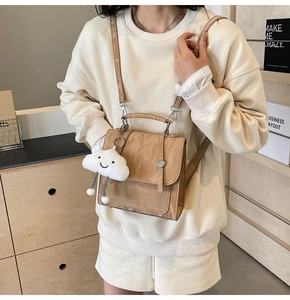 Detail of khaki pleated backpack with white plush charm and detachable straps for multi-way use