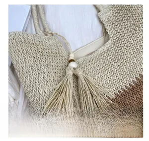 Detail of woven straw tote bag featuring contrast stitching and a stylish tassel charm