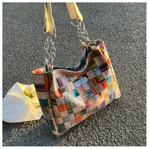Detailed view of colorful checkered tote bag featuring a metal chain handle and niche design tag