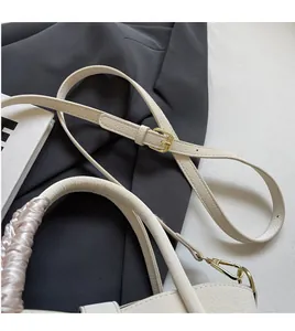 Detail of adjustable leather shoulder strap and champagne satin wrapped handle on cream tote bag