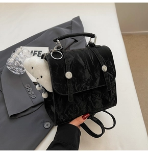 Close-up of black wrinkled patent leather backpack with silver buckles and plush charm