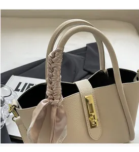 Close-up of beige lychee grain leather handbag with gold metal lock and silk scarf handle