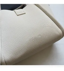 Close-up of litchi pattern leather and embossed logo detail on beige handbag