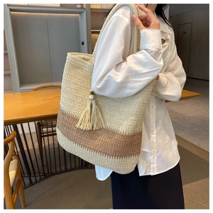 Close-up of a two-tone woven straw tote bag with fringe charm on a model's shoulder